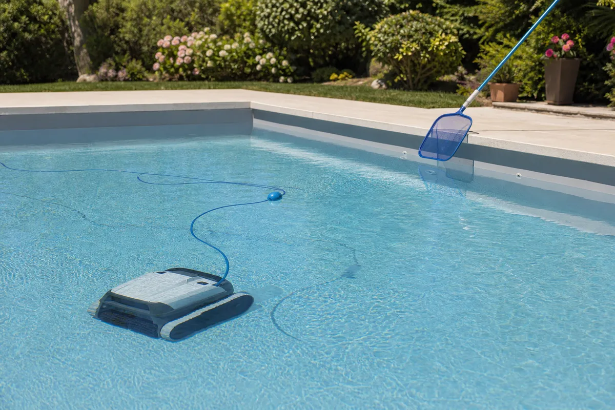Nettoyage d’un bassin de piscine au robot et à l’épuisette dans un jardin ensoleillé