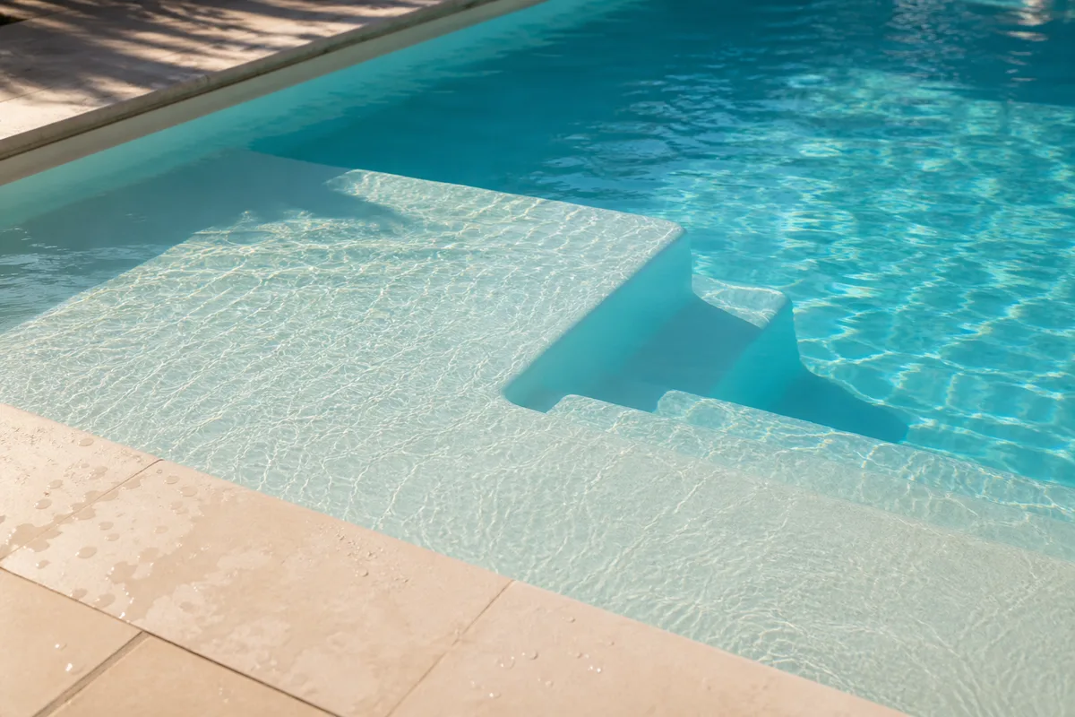 Surface gelcoat lisse d&rsquo;une piscine coque avec plage immergée sous la lumière dorée de l&rsquo;été