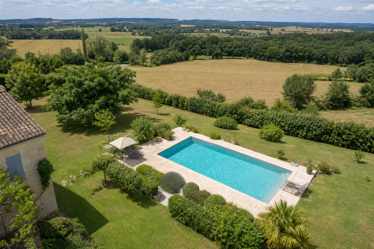 Vue aérienne d’une piscine enterrée dans un jardin arboré de la plaine du Tarn-et-Garonne sous la lumière dorée de l’été
